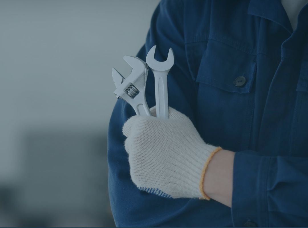 Detalhe de um profissional (mecânico/técnico) segurando duas chaves de fenda com as mãos usando luvas de proteção.